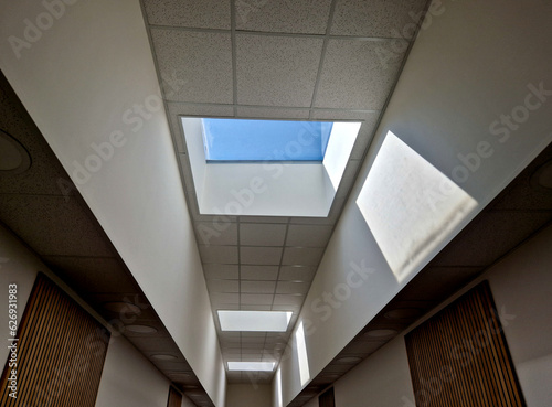 high above the head is a rectangular window illuminating the entire area of the hall with natural light. the window is a rectangular skylight. the walls are pure white plaster