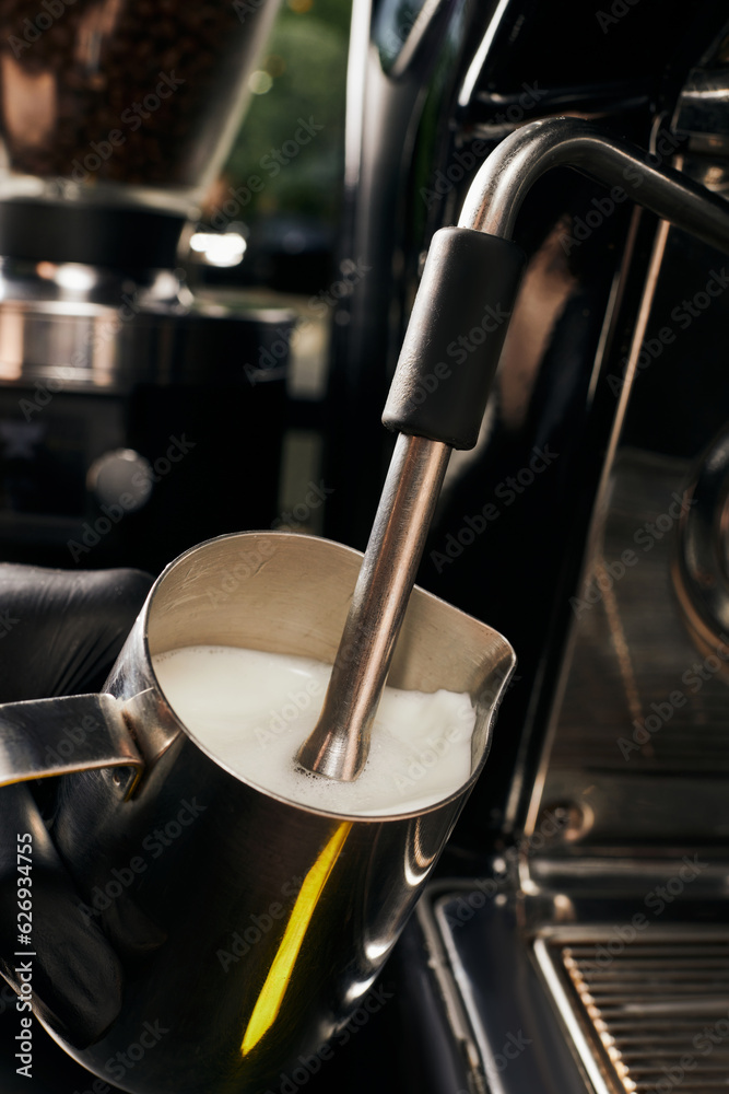 cropped view of barista frothing milk in pitcher, foaming milk, professional coffee machine, latte