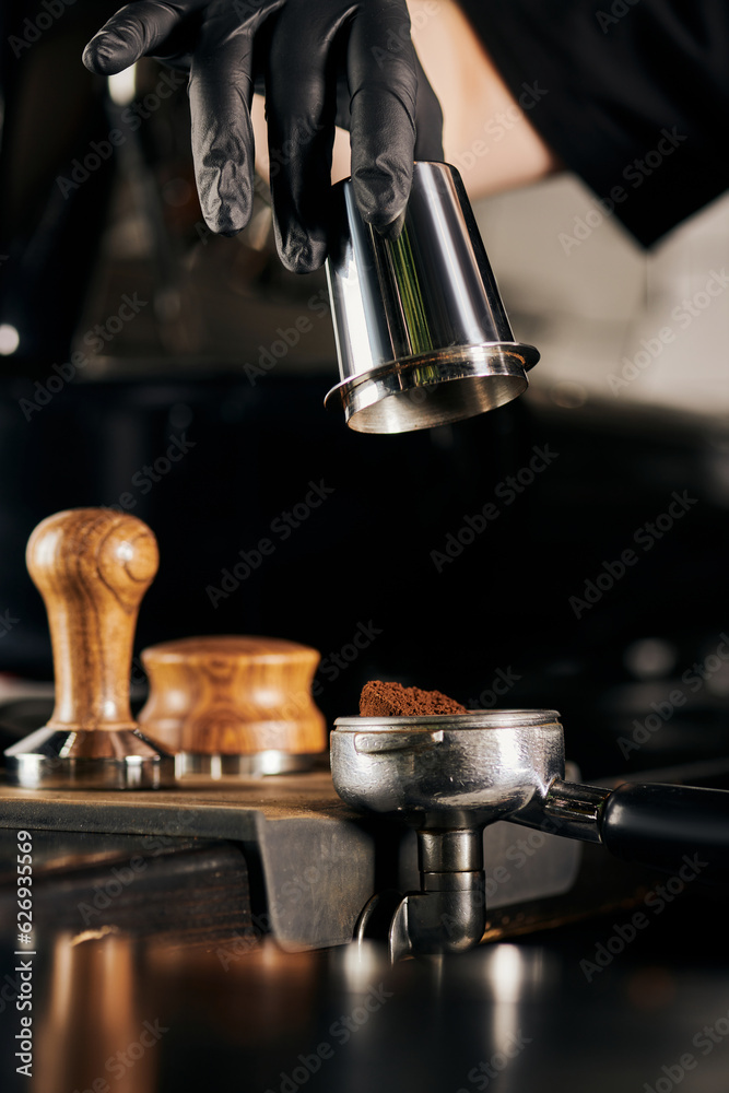 cropped view of barista in black latex glove holding measuring cup near portafilter cropped view of barista in black latex glove holding measuring cup near portafilter