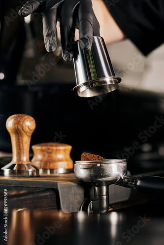 cropped view of barista in black latex glove holding measuring cup near portafilter