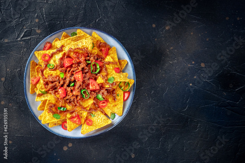 Nachos, Mexican food, tortilla chips with beef and fresh vegetables, shot from the top on a black slate background with copy space