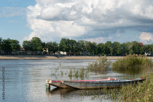 Moored boats in Sava river against city of Slavonski brod and big bright cloud in sky