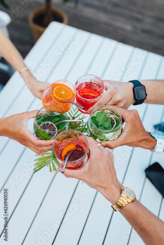 Group of friends toasting multicolored cocktails at the summer terrace