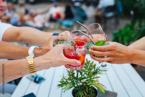 Group of friends toasting multicolored cocktails at the summer terrace