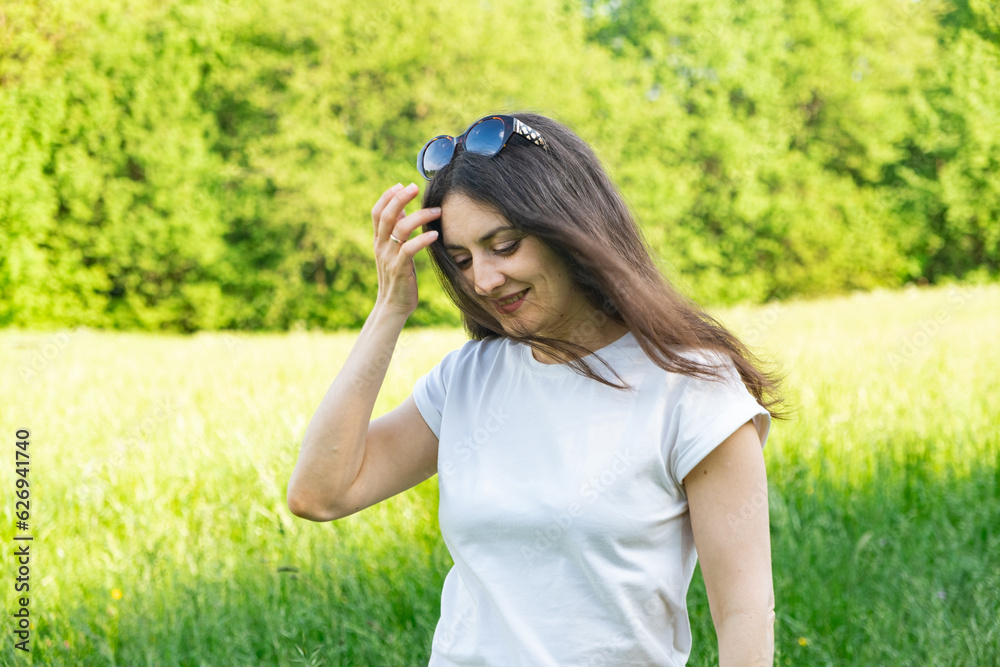 Happy 30-year-old woman straightening her hair in the wind while walking in nature in the field in summer Happy 30-year-old woman straightening her hair in the wind while walking in nature in the field in summer