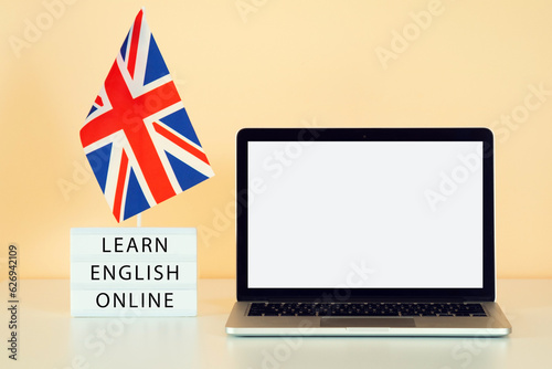 The UK flag next to a laptop with a white screen against a peach-orange wall in the apartment. Text learn english online. Mockup for banner ad about online English courses. photo