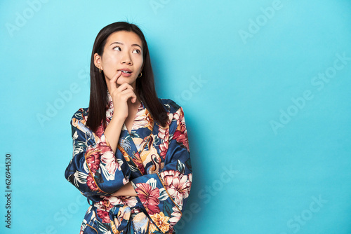Elegant young Asian woman in kimono, studio shot relaxed thinking about something looking at a copy space.