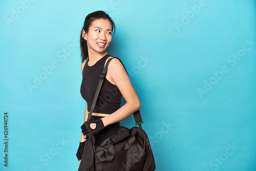 Asian woman with gym gear, ready for workout session, looks aside smiling, cheerful and pleasant.