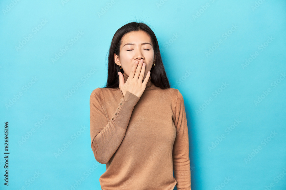 Young Asian woman in brown turtleneck, yawning showing a tired gesture covering mouth with hand. Young Asian woman in brown turtleneck, yawning showing a tired gesture covering mouth with hand.