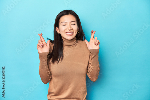 Young Asian woman in brown turtleneck, crossing fingers for having luck photo