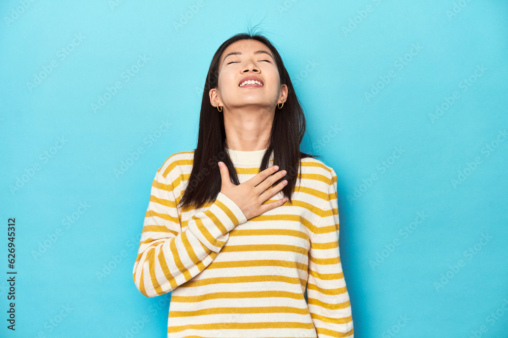 Asian woman in striped yellow sweater, laughs out loudly keeping hand on chest. Asian woman in striped yellow sweater, laughs out loudly keeping hand on chest.