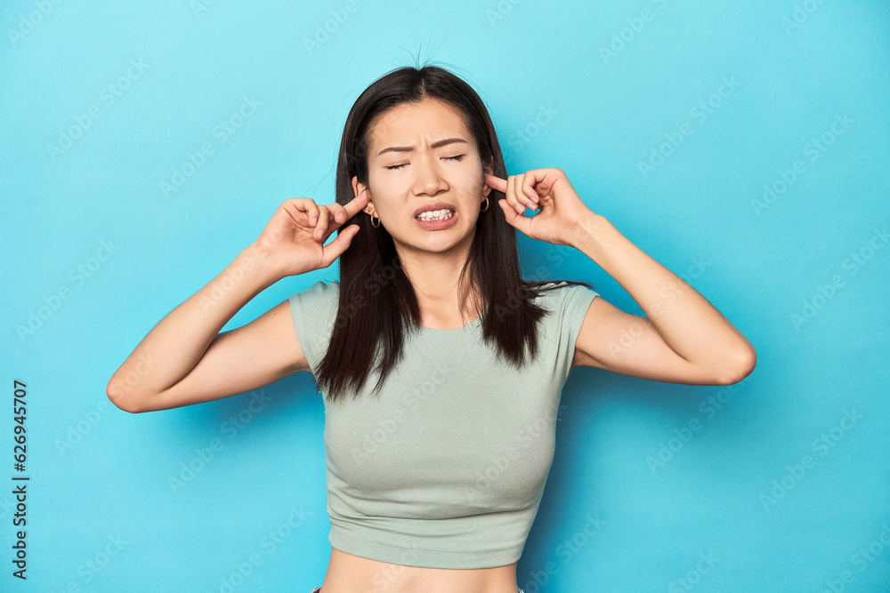 Asian woman in summer green top, studio backdrop, covering ears with fingers, stressed and desperate by a loudly ambient. Asian woman in summer green top, studio backdrop, covering ears with fingers, stressed and desperate by a loudly ambient.