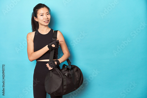 Asian sportswoman holding gym backpack, studio shot.
