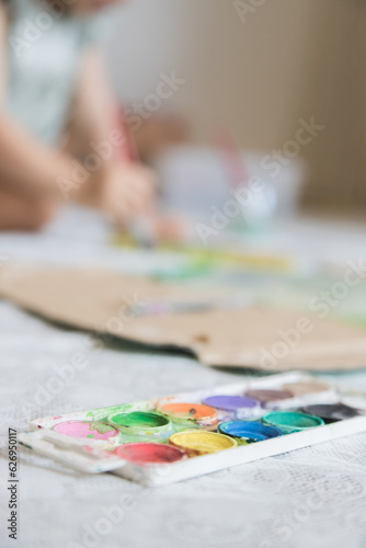 Sweet little girl playing with paints. Child exploring his creativity by painting with watercolors in a home environment. Focus on foreground.
