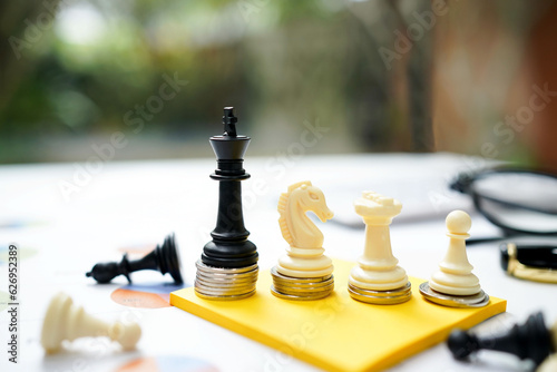 The chess business game for investment, investor competition concept in the modern style. Chess with the coin and money and some plan for business investment on yellow paper