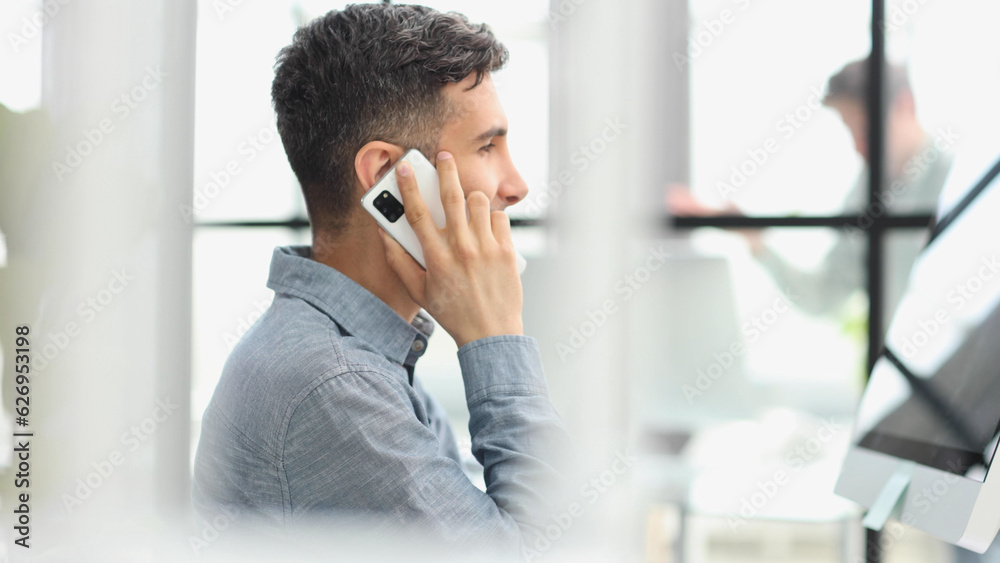 Portrait of young entrepreneur in casual office making phone call while working with laptop Portrait of young entrepreneur in casual office making phone call while working with laptop