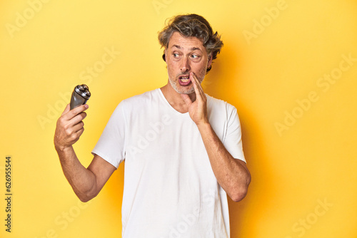 Man holding a razor, yellow studio background is saying a secret hot braking news and looking aside