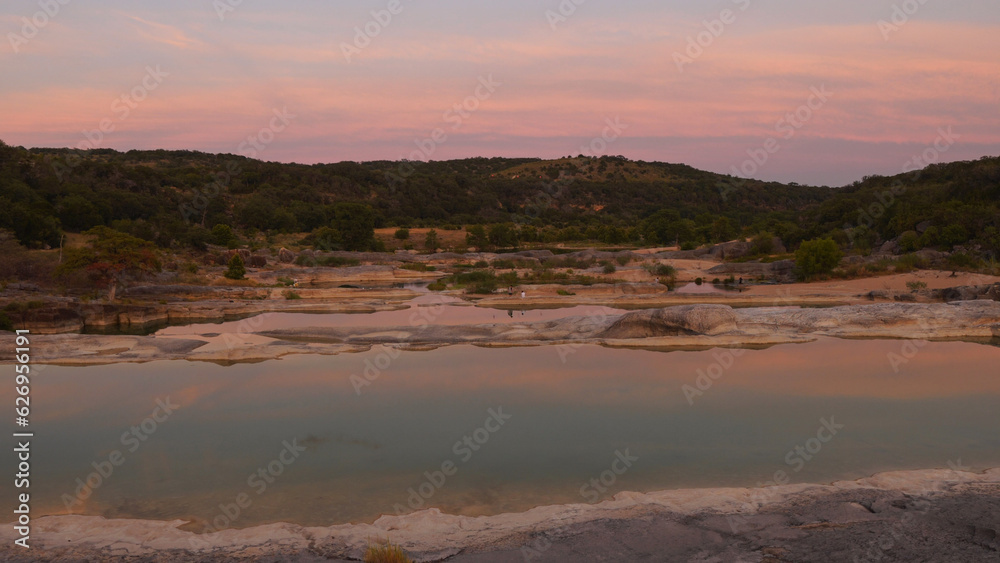 Pink and orange sky reflects on water during sunset at Pedernales Falls State Park, Texas