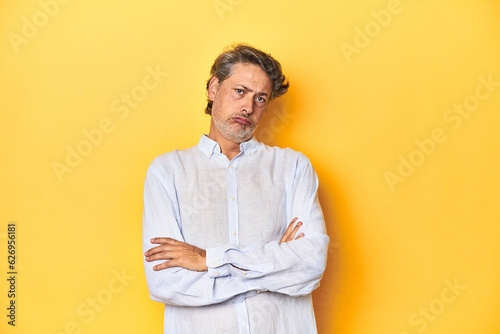 Middle-aged man posing on a yellow backdrop tired of a repetitive task.