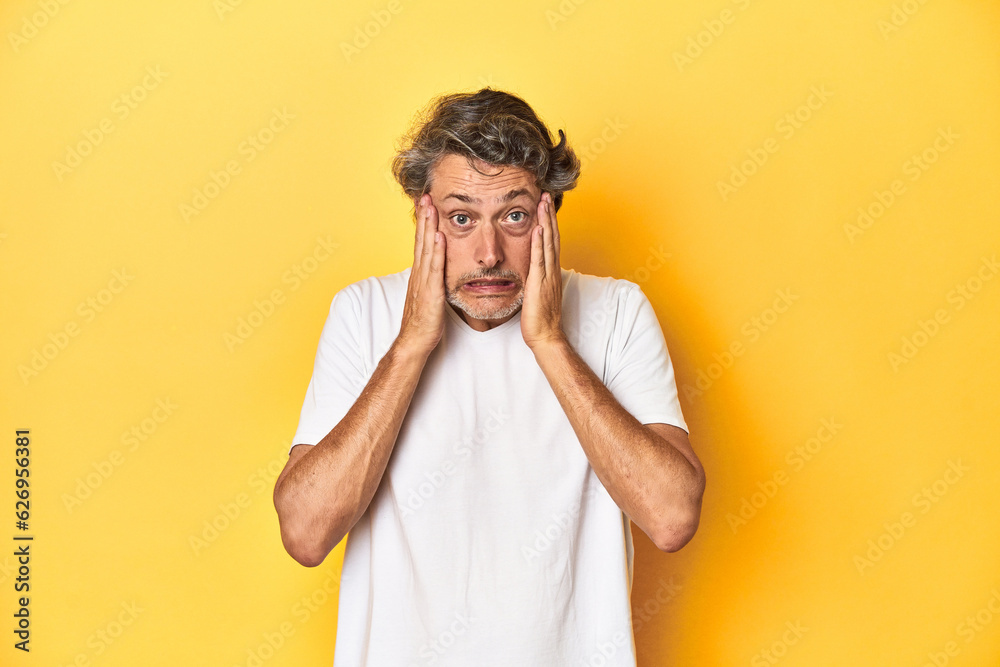 Middle-aged man posing on a yellow backdrop whining and crying disconsolately. Middle-aged man posing on a yellow backdrop whining and crying disconsolately.