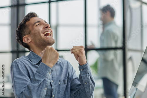 Fotografi Happy businessman rejoicing success at workplace in office, looking at laptop screen with euphoric expression