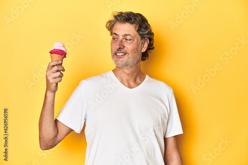 Delighted middle-aged man enjoying a refreshing ice-cream against a yellow backdrop.