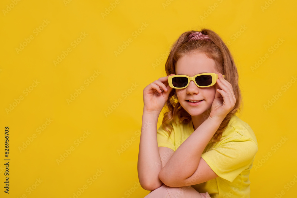 happy preteen girl in yellow t-shirt and sunglasses on yellow background. blonde girl with hairstyle high tail
