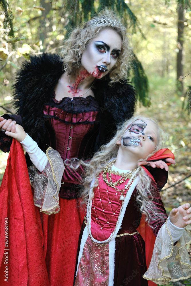 A woman in the form of a vampire or a sorceress poses in the forest with a girl in fairy-tale makeup and medieval dress. Image for Halloween