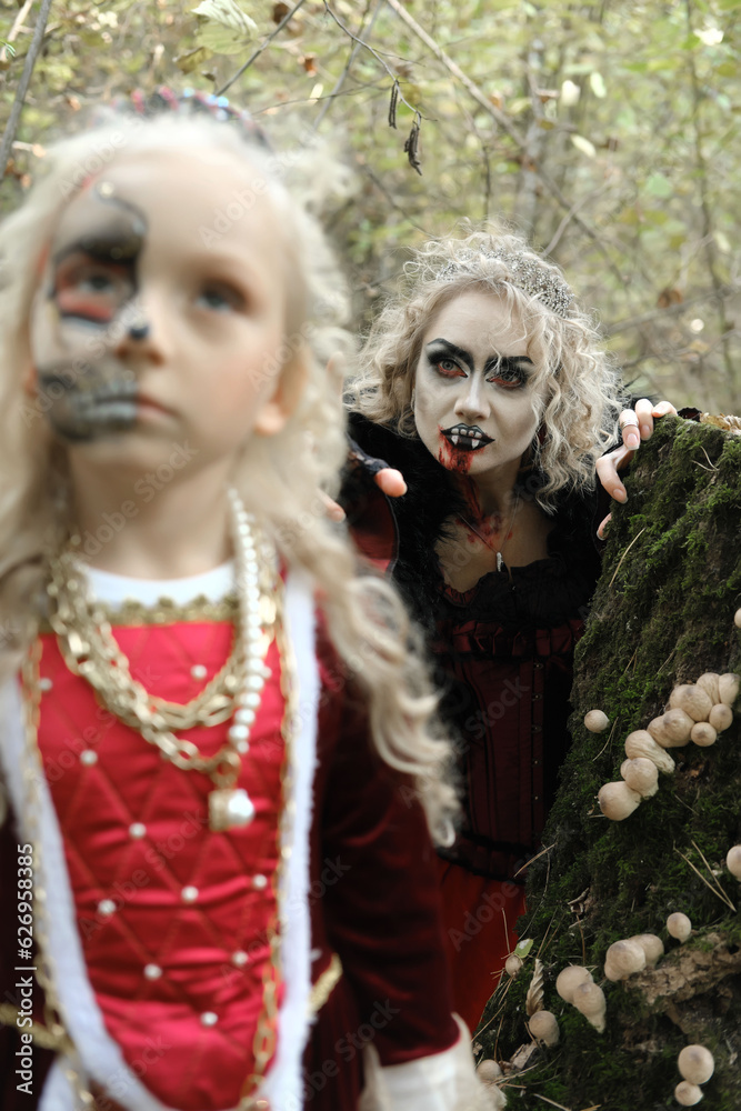 A woman in the form of a vampire or a sorceress is about to bite a princess girl in fairy-tale makeup and medieval dress. The witch is watching the girl. Image for Halloween. Focus on woman. A woman in the form of a vampire or a sorceress is about to bite a princess girl in fairy-tale makeup and medieval dress. The witch is watching the girl. Image for Halloween. Focus on woman.