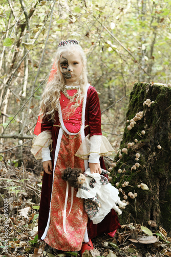 Girl child posing in the forest in a medieval dress in the image of a dead princess. Girl holding a doll