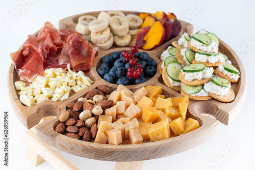 Cheeses of various types, nuts, jamon, canapes and fruits on a wooden wine table.