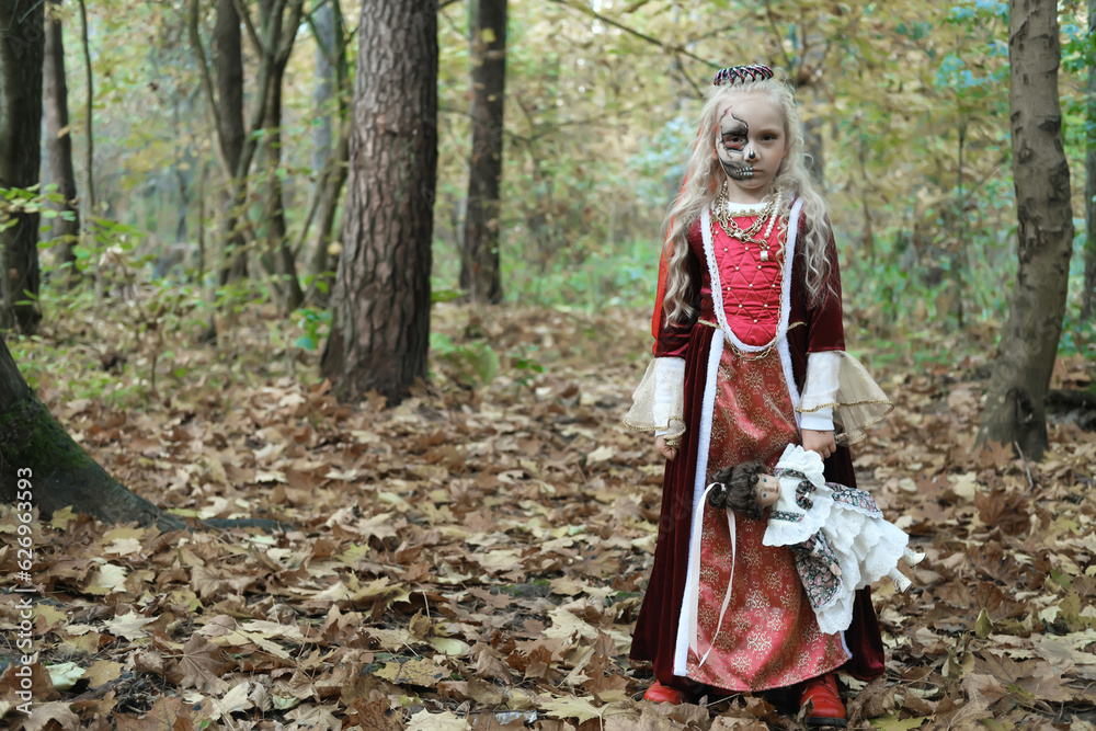 Girl child posing in the forest in a medieval dress in the image of a dead princess. Girl holding a doll Girl child posing in the forest in a medieval dress in the image of a dead princess. Girl holding a doll