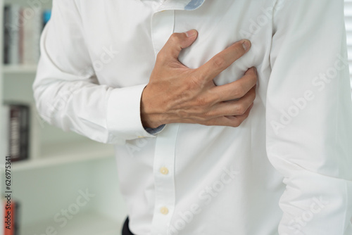 hand hold chest with heart attack symptoms, asian man working hard have chest pain caused by heart disease, leak, dilatation, enlarged coronary heart, press on the chest with a painful expression.
