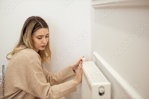 Woman warming hands on heating radiator near white wall