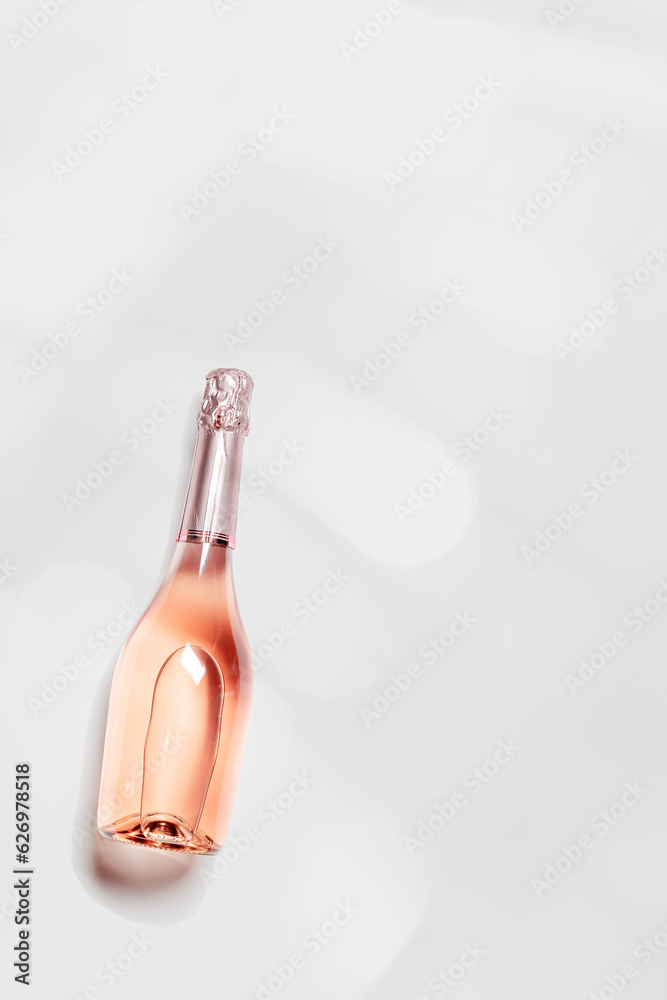 Fototapeta premium Top view sparkling rose wine with sun shadow and glare, romance beverage, bottle of champagne on light white gray background with copyspace. Festive Summer alcohol drink concept, pastel color