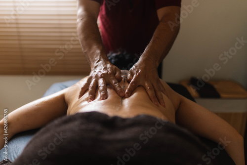 Professional anonymous man therapist standing at desk and doing massage on back of woman client