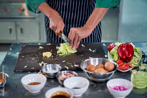 Chef is cutting vegetable on table in realistic kitchen for cooking menu.