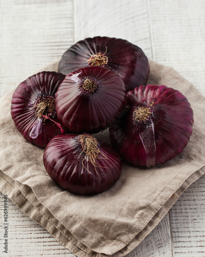 A pile of red flat onions on a napkin on a light wooden table. Vegetables.