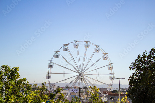 Detalhe de uma roda gigante branca, com o céu azul ao fundo.