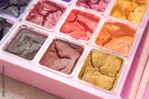 Dried colorful gouache in pink painting palette box. Cracked water color.