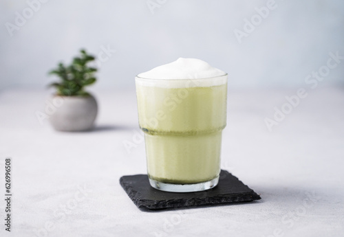 Matcha latte with ice. Green tea with milk in a glass on a light background. The concept of a traditional healthy Japanese summer refreshing drink.