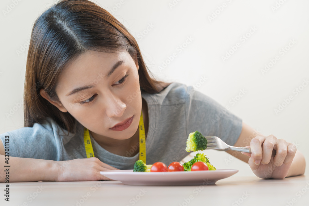 Anorexia, unhappy beautiful asian young woman, girl on dieting, hand holding fork at broccoli in salad plate, dislike or tired with eat fresh vegetables. Nutrition of clean, healthy food good taste. Anorexia, unhappy beautiful asian young woman, girl on dieting, hand holding fork at broccoli in salad plate, dislike or tired with eat fresh vegetables. Nutrition of clean, healthy food good taste.