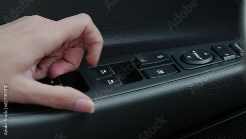 female hand turns on the car window control button on the door.