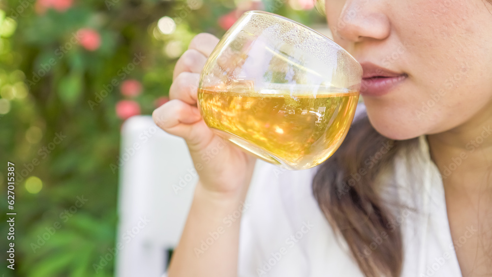A woman in white is sipping a glass of hot tea in the morning with bokeh garden backgrounds. Concept for Herbal drinks, Alternative medicine, Healthy food, Relaxation, Leisure activity. A woman in white is sipping a glass of hot tea in the morning with bokeh garden backgrounds. Concept for Herbal drinks, Alternative medicine, Healthy food, Relaxation, Leisure activity.