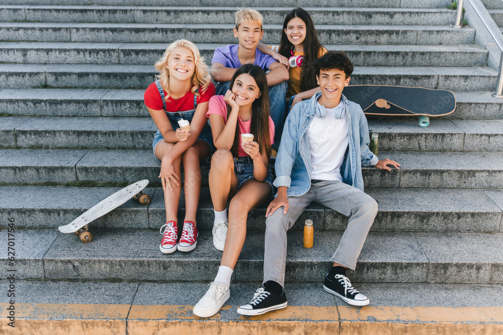 Obraz premium Smiling teenagers wearing colored t shirts sitting on stairs, eating ice cream, drinking lemonade