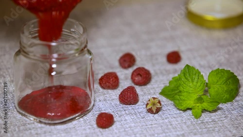 A glass jar is filled with raspberry jam. Home canning.