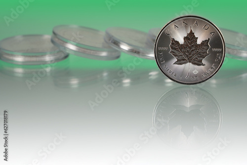 Maple Leaf silver 1 oz Ag. 9999 coin, Canada, Bullion, DNA Anti-Counterfeiting Technology, MINTSHIELD protection. In the background many silver coins. All in white green tonation.         photo