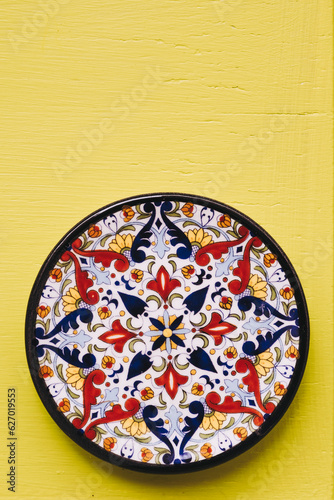 Assiette décorative en céramique colorée posée sur un mur jaune