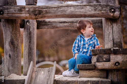 Little toddler boy in blue shirtsiting on a wooden stairs on playground
