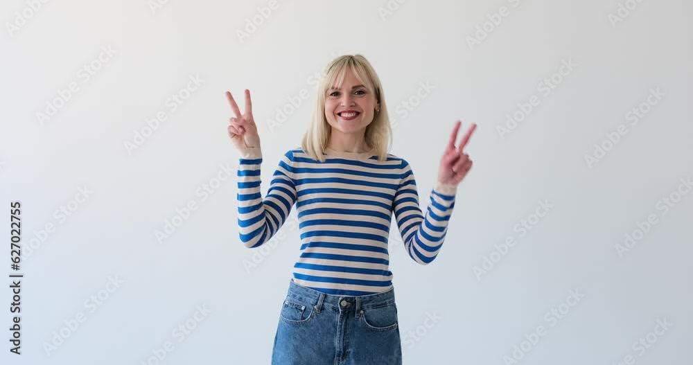 Lively and cheerful woman is seen on a clean white backdrop, making the 'V' gesture with her fingers. Her radiant smile and enthusiastic demeanor exude happiness and positivity. Lively and cheerful woman is seen on a clean white backdrop, making the 'V' gesture with her fingers. Her radiant smile and enthusiastic demeanor exude happiness and positivity.